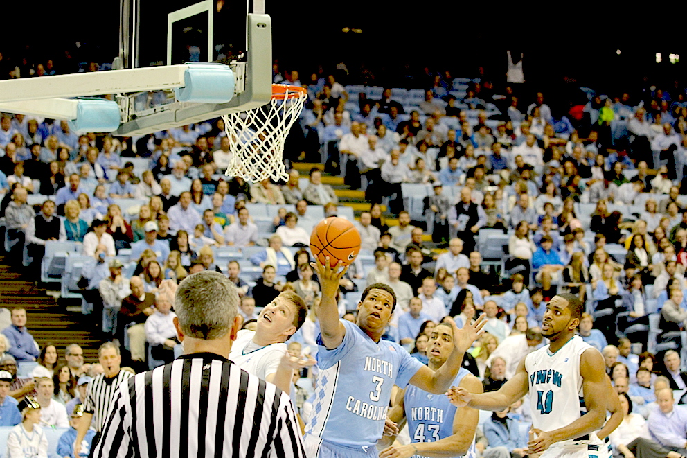 Kotijoukkue Tar Heels voitti UNC Wilmingtonin 16 923 katsojan riemuksi 84–51. Vaaleansinisessä paidassa pallon perässä Kennedy Meeks. Ottelun tähti, legendaarisen Bob McAdoon veljenpoika James M. McAdoo (nro 43) seuraa vierestä. McAdoo kerästi tässä pelissä tehot 23/10.