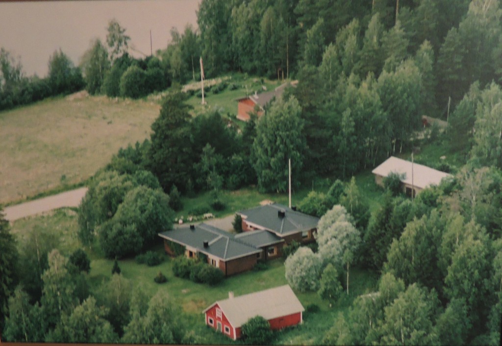 KUVATEKSTI: Ilmakuva 1970-luvulta, jolloin Voutien uusi rakennus on valmistunut, ja jäljellä on vielä vanha navetta kuvan alareunassa. Huoltoasema ja Nelostie jäävät kuvan ulkopuolelle.